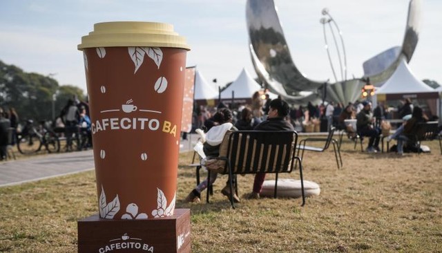 Personas disfrutando de café y pastelería en la feria Cafecito BA en la Plaza de las Naciones Unidas, con la Floralis Genérica al fondo.