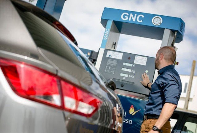 Auto estacionado junto a un surtidor de GNC con un cilindro de gas en el baúl